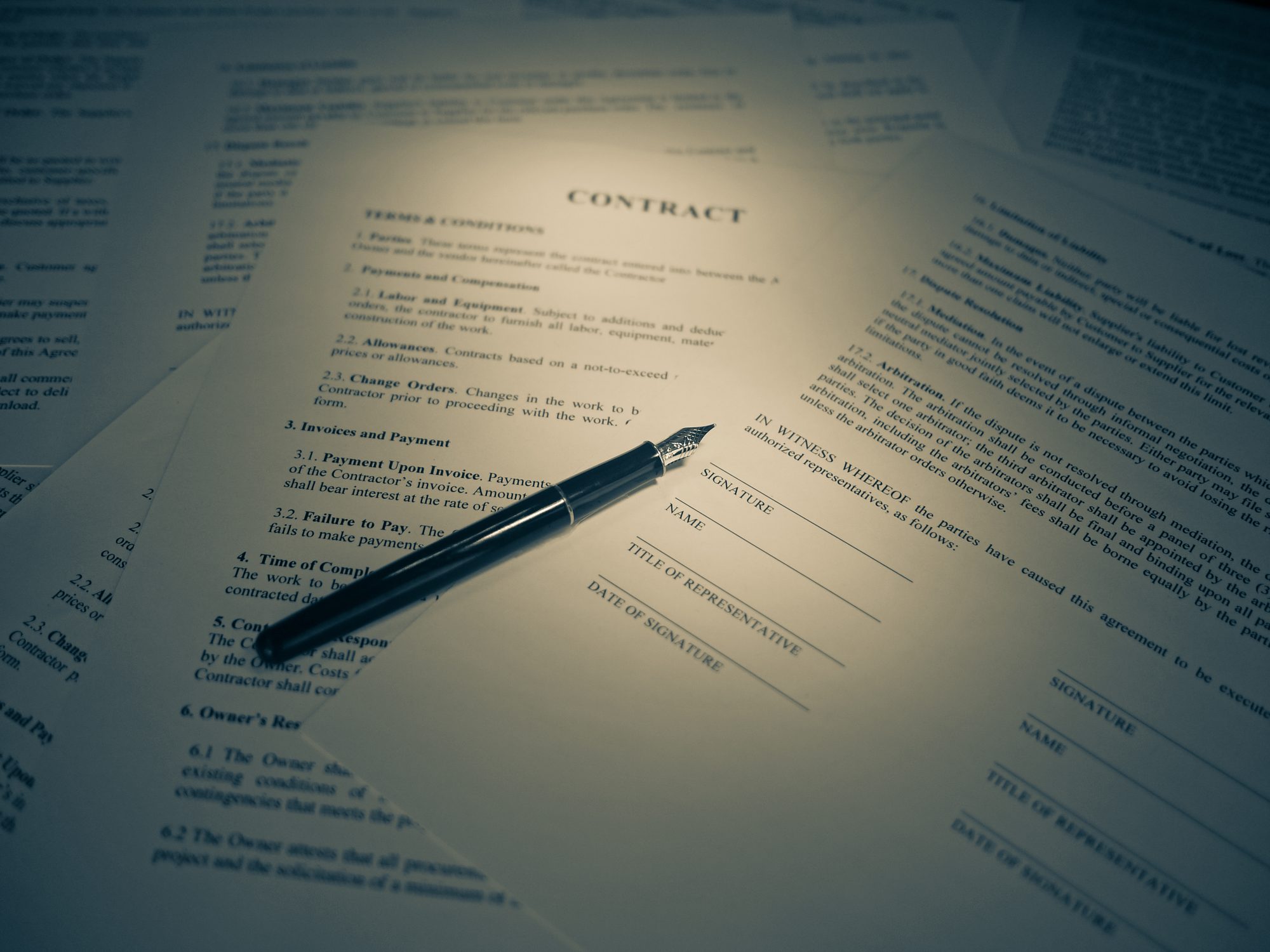 A printed contract on a desk with a pen resting across the signature page