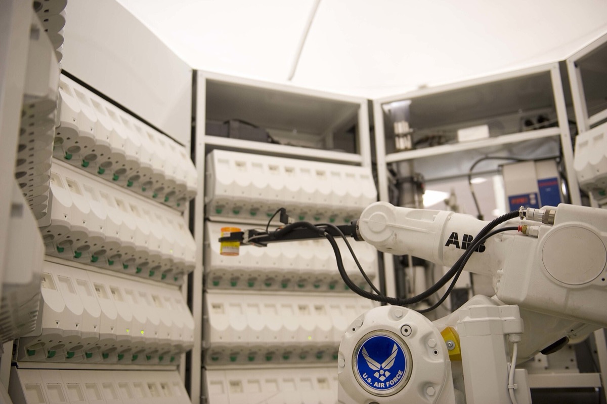 Robotic arm in an automated pharmacy dispensing system before a wall of medication cassettes